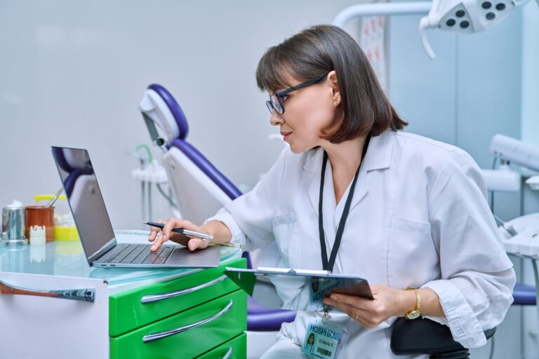 Doctor dentist working in office, using laptop, making notes on clipboard